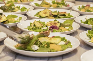 Turuncu soslu ızgara kabak ve yeşil marul yaprağında mozzarella peyniri. Masada salata olan tabaklar.