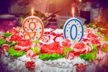 90. yıl dönümü. Çiçekler, desenler ve dokuz ve sıfır numaralarıyla süslenmiş pasta. Tatil konsepti, yanan mumlarla doğum günü. Boyama