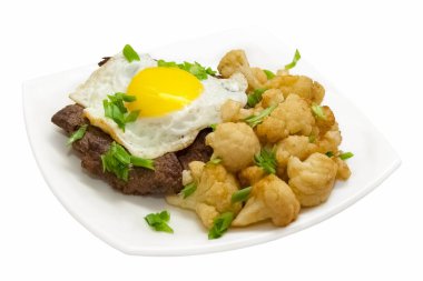 Kızarmış yumurtalı biftek ve yanında beyaz tabakta kızarmış brokoli. Ayrı nesne