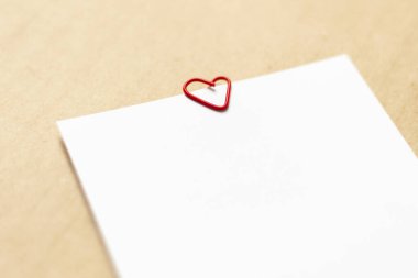 Kraft kağıdının arka planında boş beyaz çarşaflar. Kalp şeklinde kırmızı bir ataç var. Yakın plan.