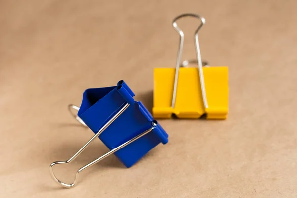 Two paper clips blue and yellow on a brown background. Close-up. Background, craft paper