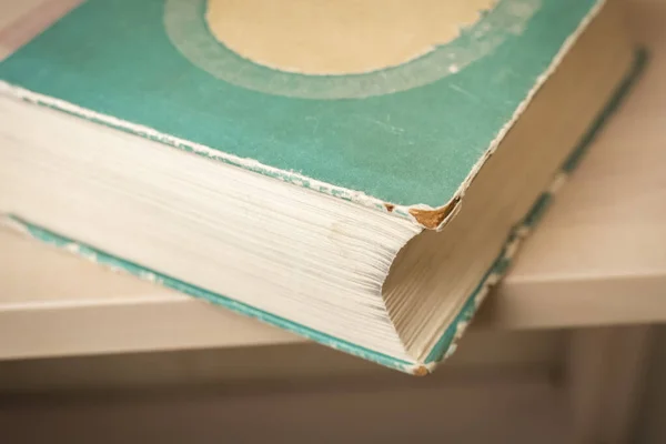 Detail of an old book, cover and page. The book is on a wooden shelf. Close-up