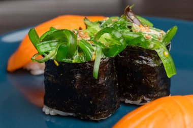 Chukka gunkan deniz yosunu suşisi ve mavi bir tabakta yuvarlanıyor. Japon yemeği servisi. Yakın plan.