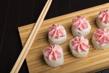 Bambu tahtasında pembe lav soslu rulo. Tahta bir masada Japon yemeği servis etmek. Yakın plan.