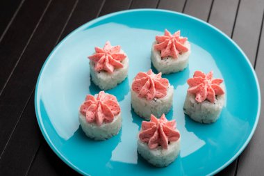 Mavi bir tabakta, ahşap bir masada pembe lav soslu rulo. Japon yemeği servisi. Yakın plan.