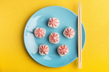 Pembe lava soslu suşi rulo pilavı mavi bir tabakta, yemek çubuklarıyla, sarı arka planda. Japon yemeği servisi. en üstteki görünüm