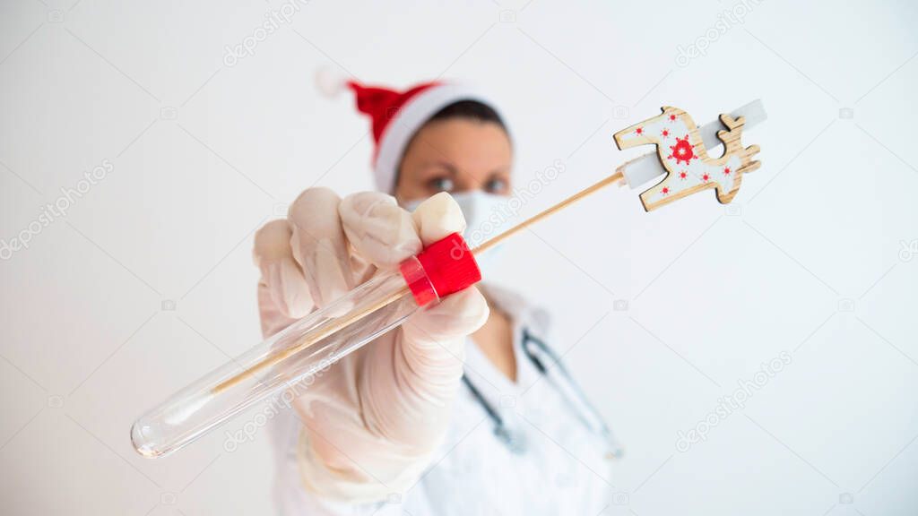 A female doctor with a Santa hat is holding medical swab for sampling on a white background. Corona virus during the holidays.