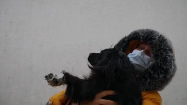 Sarı ceketli, tıbbi maskeli bir kadın köpeğini kollarında tutuyor..