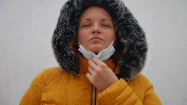 Sarı ceketli bir kadının yakın plan portresi gözlerini kapatıyor, yüzündeki cerrahi maskeyi çıkarıyor ve derin bir nefes alıyor. Grip, koronavirüs veya hava kirliliğinin önlenmesi.