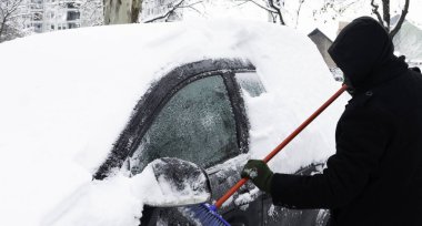 Adam fırçayı kullanarak arabanın karını kazıyor..