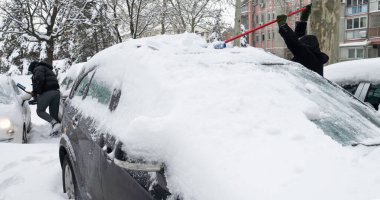 Tanınmayan insanlar kar fırtınasında karla kaplı arabayı temizliyorlar..