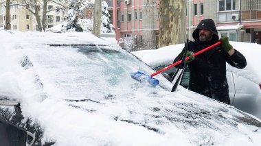 Ön arabanın camındaki karları temizleyen adam uzun bir fırça..