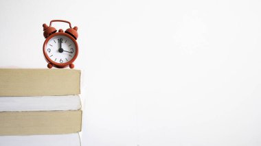 Kitapların üstündeki kırmızı saat saat 12 'yi gösterir - metin için negatif boşluk veya kopyalama alanı.