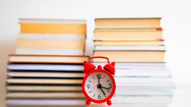 Bir masanın üzerinde kırmızı bir saat ve bir defterin arkaplanı.