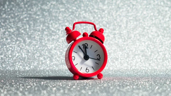 Red clock on a silver glitter background.