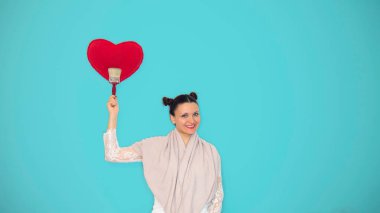 Büyük fırçalı mutlu kadın mavi duvara kırmızı bir kalp çiziyor. Metin için alanı kopyala.