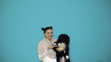 Mavi arka planda siyah bir köpeği kollarında tutan gülümseyen beyaz bir kadın..