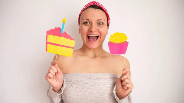 Woman with fake paper craft cake and muffin on a stick liking her lips. A portrait of a happy woman who likes to eat sweets.