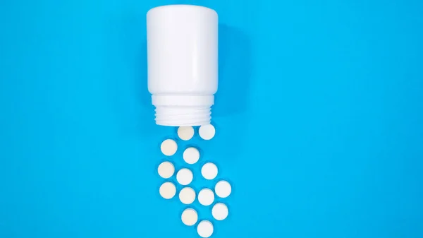 Pills spilling out of white pill bottle on blue background. Negative space for text. Medicine concept