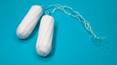 Mavi arka planda iki tıbbi tampon. Kadınlar için hijyenik beyaz tampon. Pamuklu çubuk. Regl, korunma aracı. 