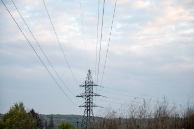 Yüksek voltajlı elektrik hatları ve bulutlu bir gökyüzüne karşı elektrik direği. Endüstriyel enerji altyapısı