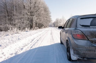 Uzak bir kırsal yolda, derin kar izleri olan kirli, donmuş bir arabanın yakın çekimi. Tehlikeli sürüş koşulları, dondurucu hava ve kötü kış yolu bakımı kavramı