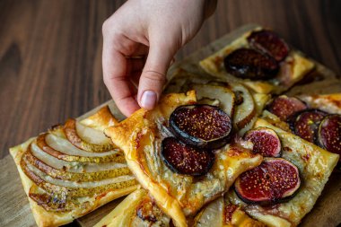 İncir ve ahşap bir tahtanın üzerinde dilimlenmiş armutla kaplı ev yapımı puf börekleri. Sıcak ve sıcak bir atmosferde altın kabuklar ve sulu meyveler. Pişirme, tatlı ya da sonbahar yemeği kavramları için mükemmel..