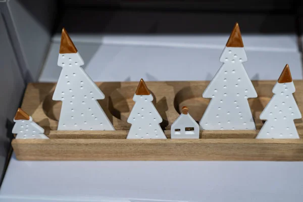 Beyaz seramik ağaçlar ve ahşap tabanlı küçük bir ev içeren basit ve zarif bir Noel kompozisyonu. Temiz tasarım ve sıcak tonlar, modern iç mekan veya festival pazarlama görselleri için mükemmel bir tatil duygusunu çağrıştırıyor..