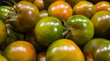 Yeşil, kırmızı ve kehribar rengi de dahil olmak üzere çeşitli doğal renklerdeki domateslerin yakın çekim görüntüsü. Görüntü, canlı dokular ve organik ayrıntılarla bir pazar yerinde taze ürünleri ön plana çıkarıyor.