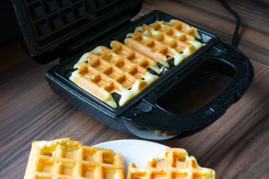 Kalın waffle hamuru waffle ızgarasının içinde ısınmaya başlar ve kenarlarında altın bir kabuk oluşturur. Görüntü, ev yapımı waffle hazırlığının ilk aşamasını yakalıyor. Yumuşak tonlar dokuyu ve ısıyı vurgular.