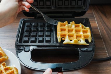 Waffle makinesinden çatalla tek bir waffle kaldırılır. Sahne, ev yapımı bir kahvaltının dokusunu ve sıcaklığını ön plana çıkarıyor. Aşçılık medyası için ideal.