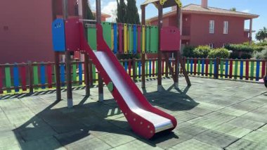 Açık alanda renkli çitleri olan çocuklar kırmızı kaydırak kullanıyor.. 