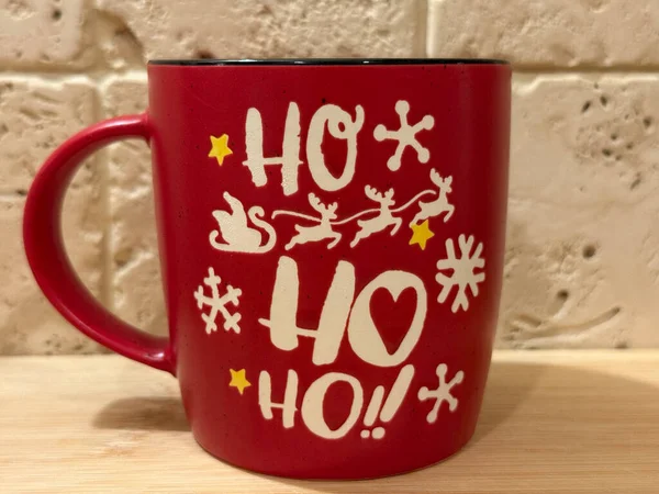Red Christmas mug with Ho Ho Ho print on wooden table. 