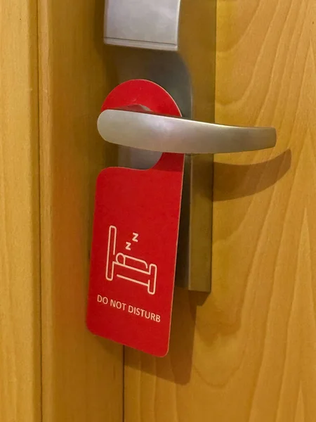 red do not disturb sign hanging on a silver door handle of a wooden door