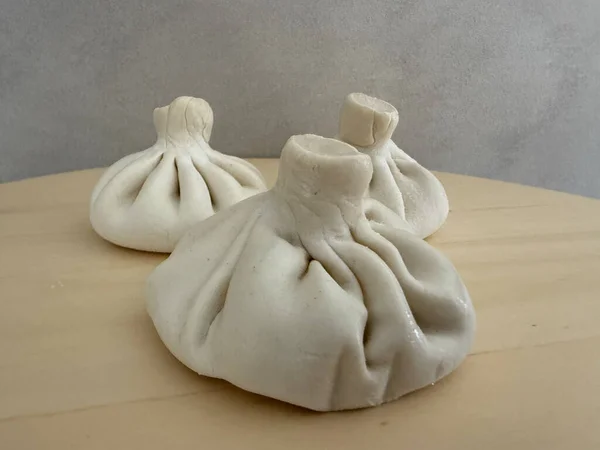 three uncooked georgian khinkali dumplings on a light wooden board with a grey background