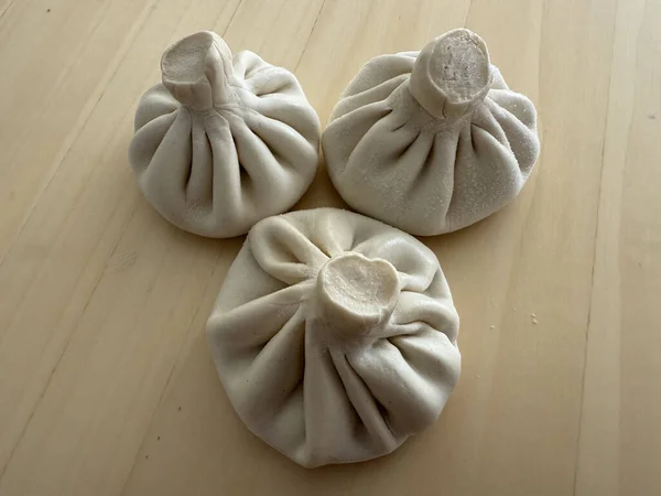 three uncooked khinkali dumplings on a light wooden surface. concept of georgian cuisine.