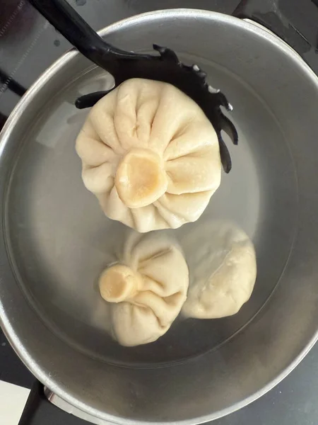 khinkali dumplings being cooked in a metal pot on a stovetop, traditional georgian food