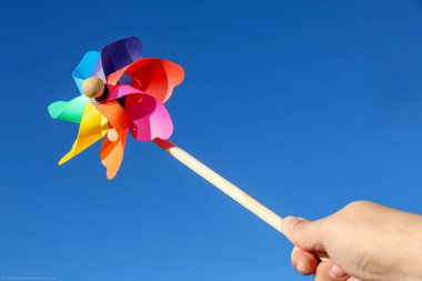 Mavi gökyüzüne karşı bir insanın elinde renkli bir fırıldak