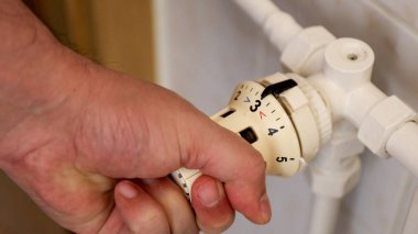 Sıcaklığı ayarlamak için termostat kullanan bir adamın eli.