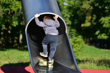 Küçük çocuk parlak bir oyun parkına tırmanmaya çalışıyor. Hareket ve yerçekimini keşfediyor. Erken çocukluk macerası ve parlak gün ışığında merak.