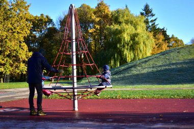 Babam çocuklarla kırmızı halatla oynuyor. Güneşli bir sonbahar sabahı parkta tırmanıyor. Aile birlikte dışarıda eğleniyor. İki çocuklu baba dışarıda eğleniyor.