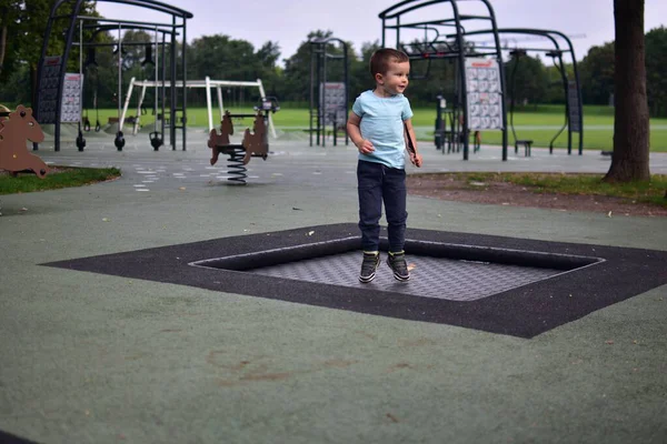 Çocuk, elinde tüy tutarak çocuk parkının içinde trambolinde zıplıyor. Yeşil park çevresindeki doğa hareketi ve enerji anı..