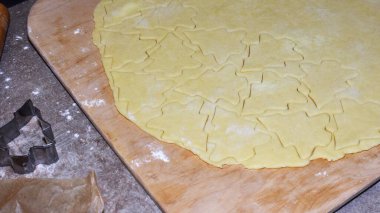 Çiğ kurabiye hamuru ahşap bir tahtanın üzerine yuvarlanmış ve metal kurabiye keskisi kullanılarak kesilmiş Noel ağacı şekilleri var. Bayram kurabiyeleri için pasta hazırlama sahnesi..