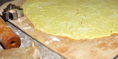 Kurabiye hamuru tahta bir tahtanın üzerine yuvarlandı ve Noel ağacı şeklinde kesildi. Yakınlarda bir metal kesici ve merdane var. Evde tatil kurabiyeleri hazırlama sürecini gösteriyor..