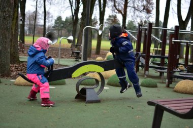 Sonbahar parkında birlikte oynayan iki çocuk tahterevalli. Sıcak kış kıyafetleri içindeki çocuklar işbirlikçi açık hava oyunları, denge ve sosyal becerileri öğrenmekten hoşlanırlar..
