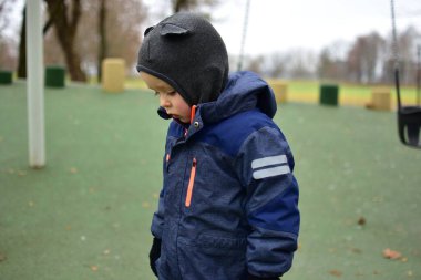 Çocuk portresi, okul bahçesinde duran kışlık ceketli çocuk portresi. Sonbahar parkında sakin bir havada eğlenirken çocuk düşünceli görünüyor. Sakin ve üzgün görünümlü bir çocuk sonbahar günü dışarıda yürüyor..