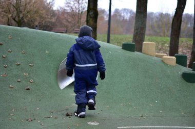Çocuk oyun tepesine inşa edilmiş oyun parkı tüneline yaklaşıyor. Çocuk, sonbahar parkında dışarıda oynarken tırmanma ve sürünme fırsatlarını keşfediyor..