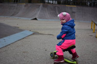 Sonbaharda kaykay parkında dengeli bisiklete binen küçük bir kız. Sıcak kış giysileri giyen, aktif oyun ve erken çocukluk hareketliliği yoluyla denge ve koordinasyon geliştiren çocuk.