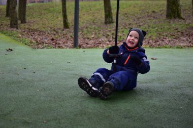 Sonbahar parkında elinde iple oyun parkında oturan mutlu çocuk. Erken çocukluk aktivitelerinde kalın kışlık giysiler giyen, denge, koordinasyon ve motor becerileri geliştiren çocuk.