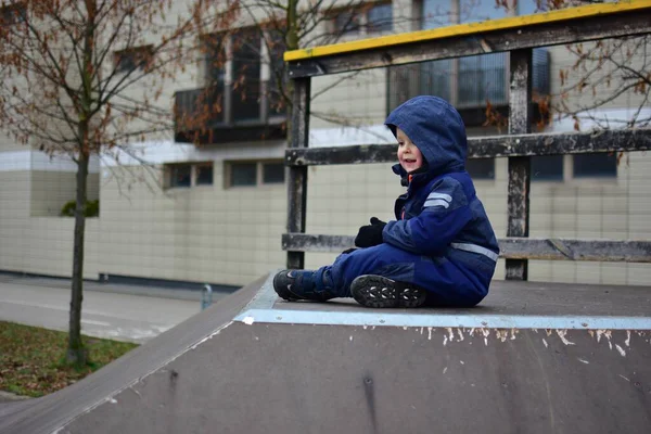 Sonbahar boyunca şehir parkında kaykay rampasının tepesinde oturan küçük çocuk. Sıcak kışlık giysiler giyen çocuk, sakin bir açık hava anının tadını çıkarıyor, çocukluğunda kendine güven ve bağımsızlık kazanıyor..